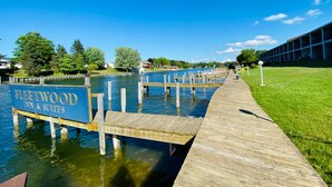 A wooden dock leading to a boat named 'Fleetwood Inn & Suites' with a clear view of the water and a building in the background.