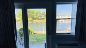 A room with a sliding glass door leading to a patio with a view of a lake and a house across the water.