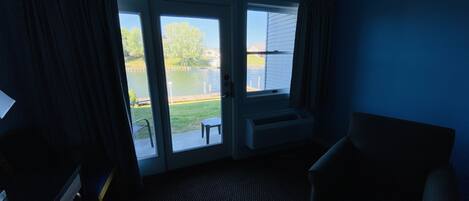 A room with a view of a lake, a chair, a table, and a heater.