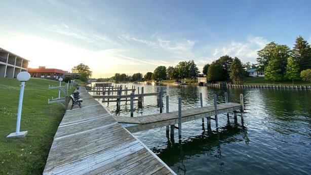 A wooden dock extending into a calm body of water, surrounded by grassy areas and trees.