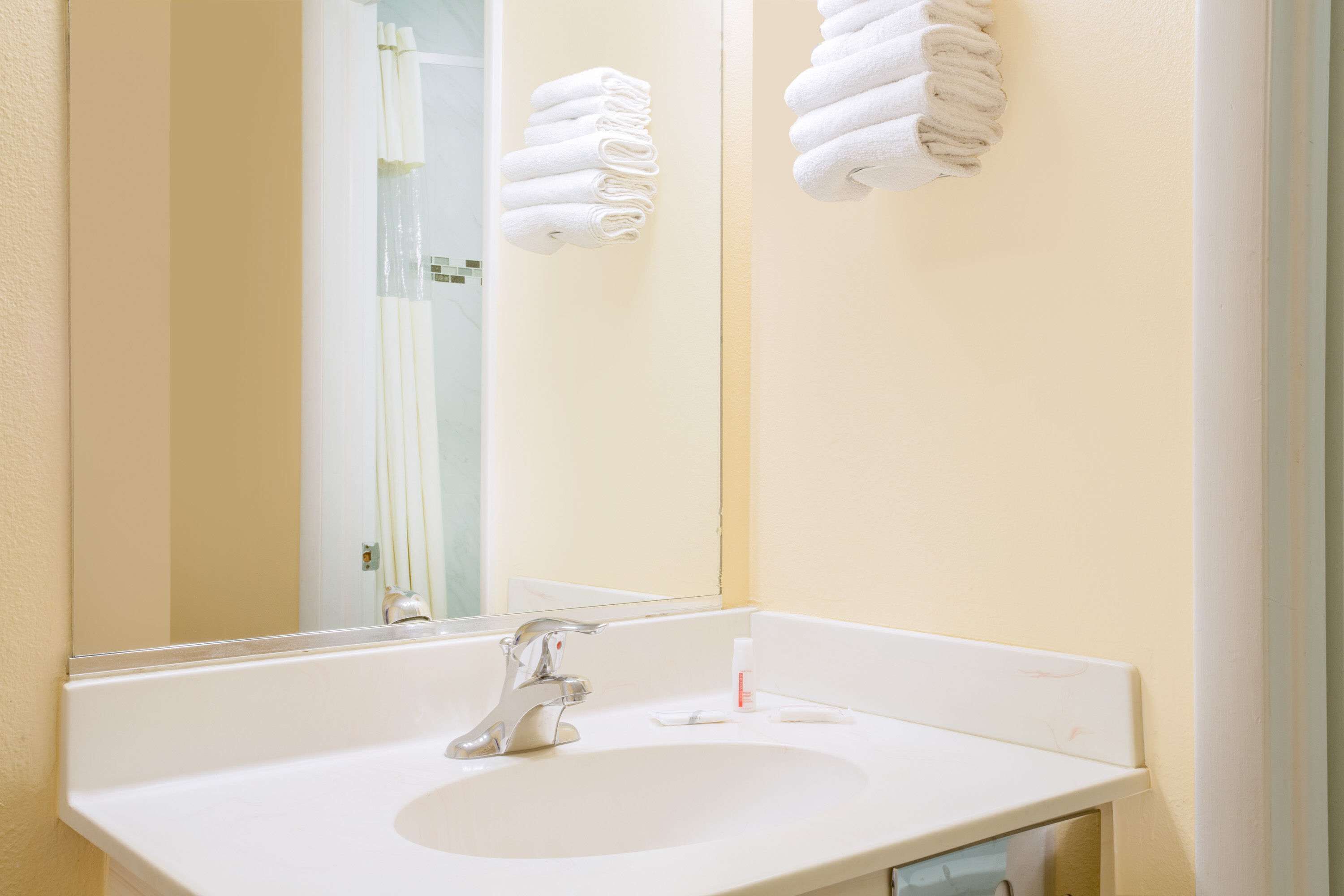 A bathroom with a white sink, a mirror, and two towels hanging on the wall.