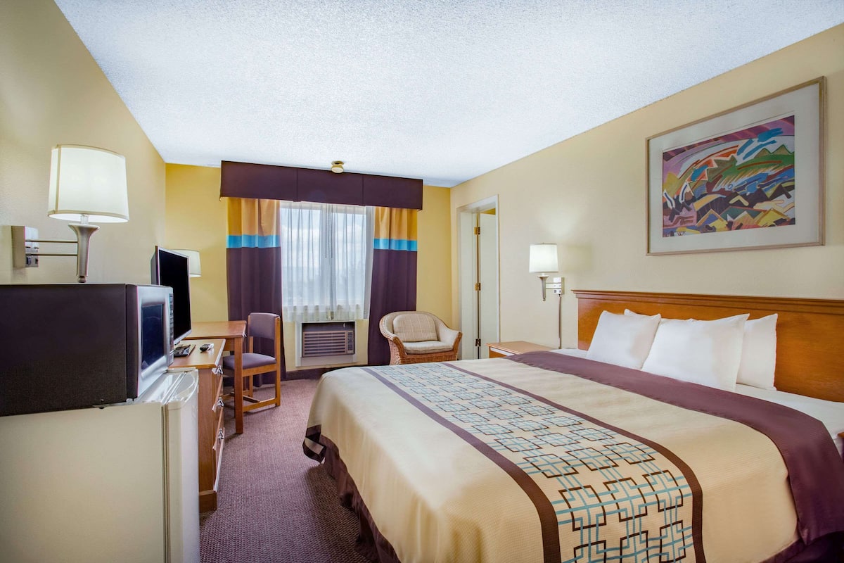 A hotel room with a bed, a desk with a computer, a chair, a television, and a painting on the wall.