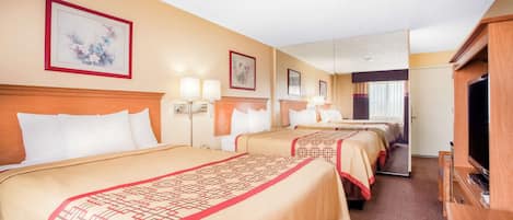 A hotel room with three beds, a television, and a mirror.