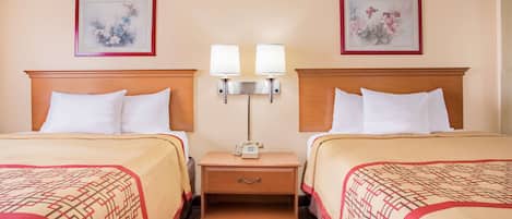 Habitación de hotel con dos camas, una mesita de noche con lámpara y dos cuadros enmarcados con motivos florales en las paredes.