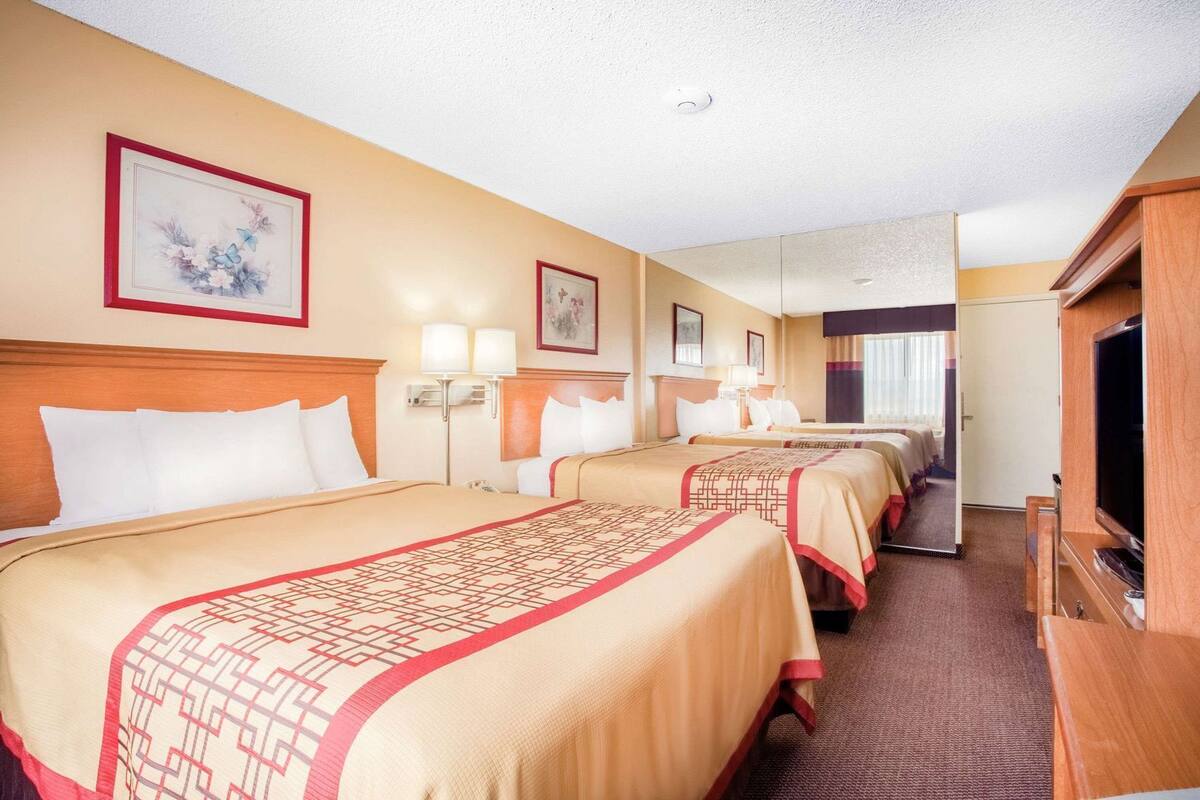 A hotel room with three beds, a TV, and a mirror.