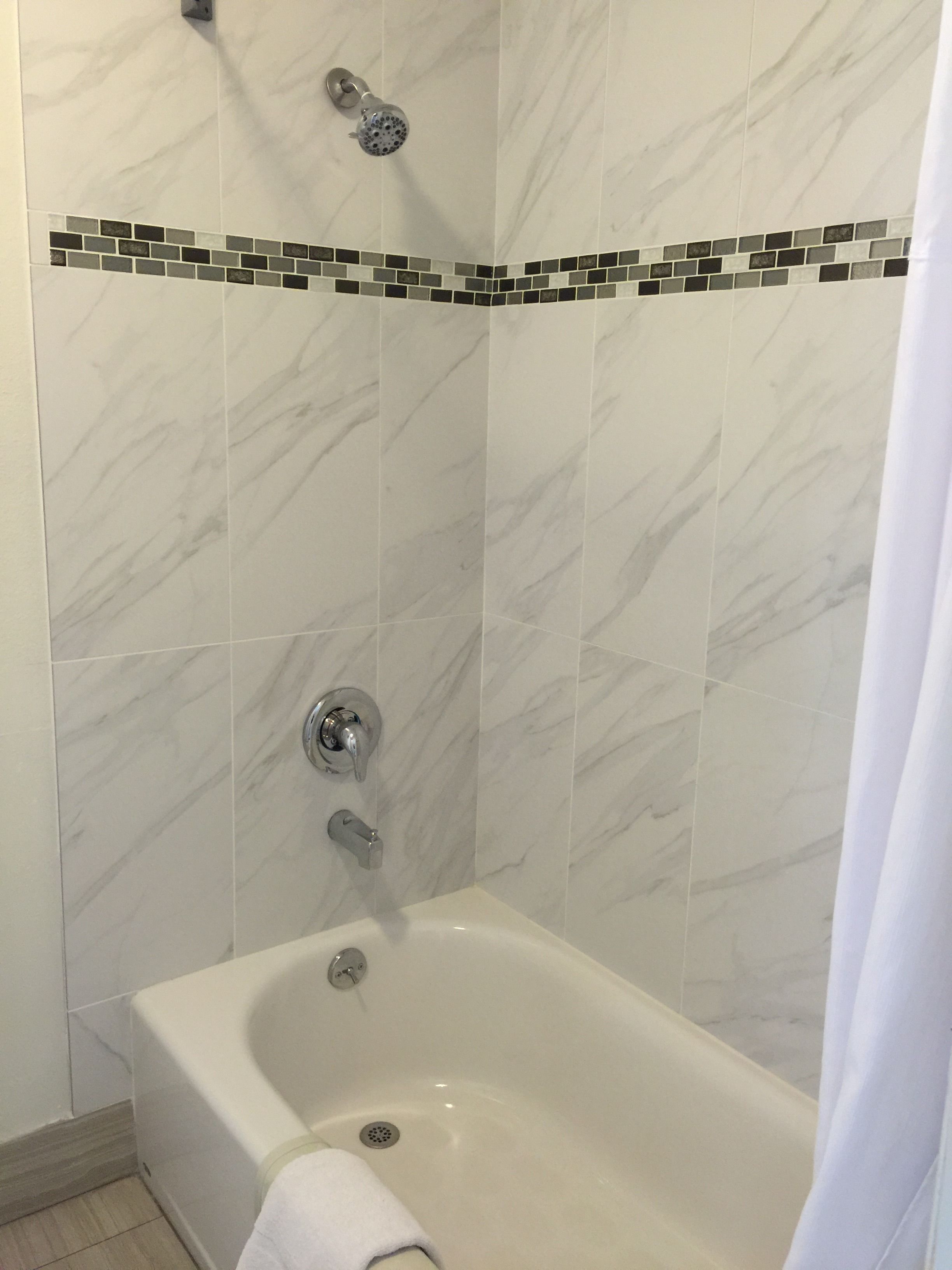 Et badeværelse med badekar, brusehoved og en flisevæg med mosaik kant.