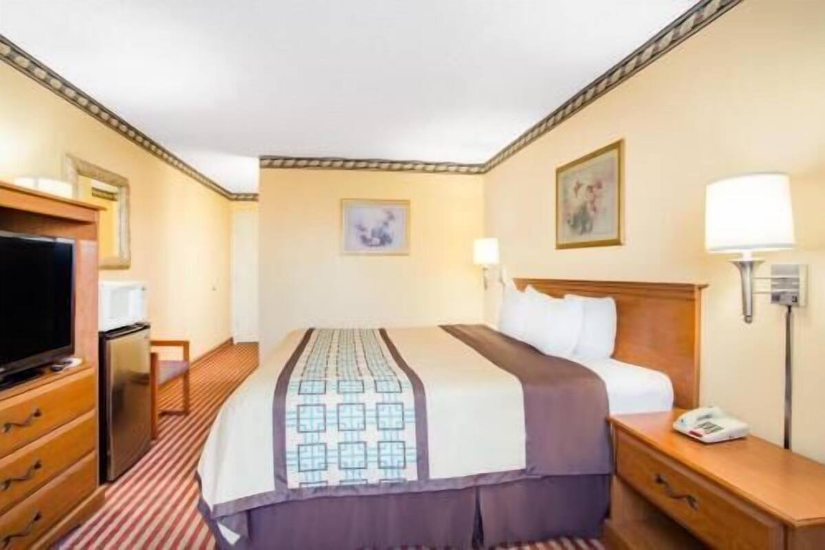 A hotel room with a bed, bedside table, lamp, television, and a desk with a chair.