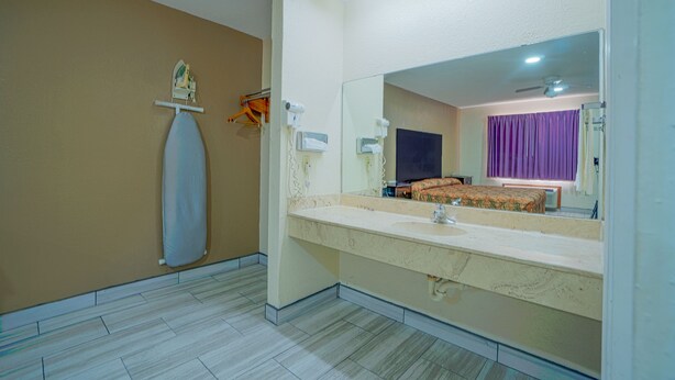 A bathroom with a large mirror, a sink, and a shower area. - Texas Inn San Benito near Harlingen (San Benito)