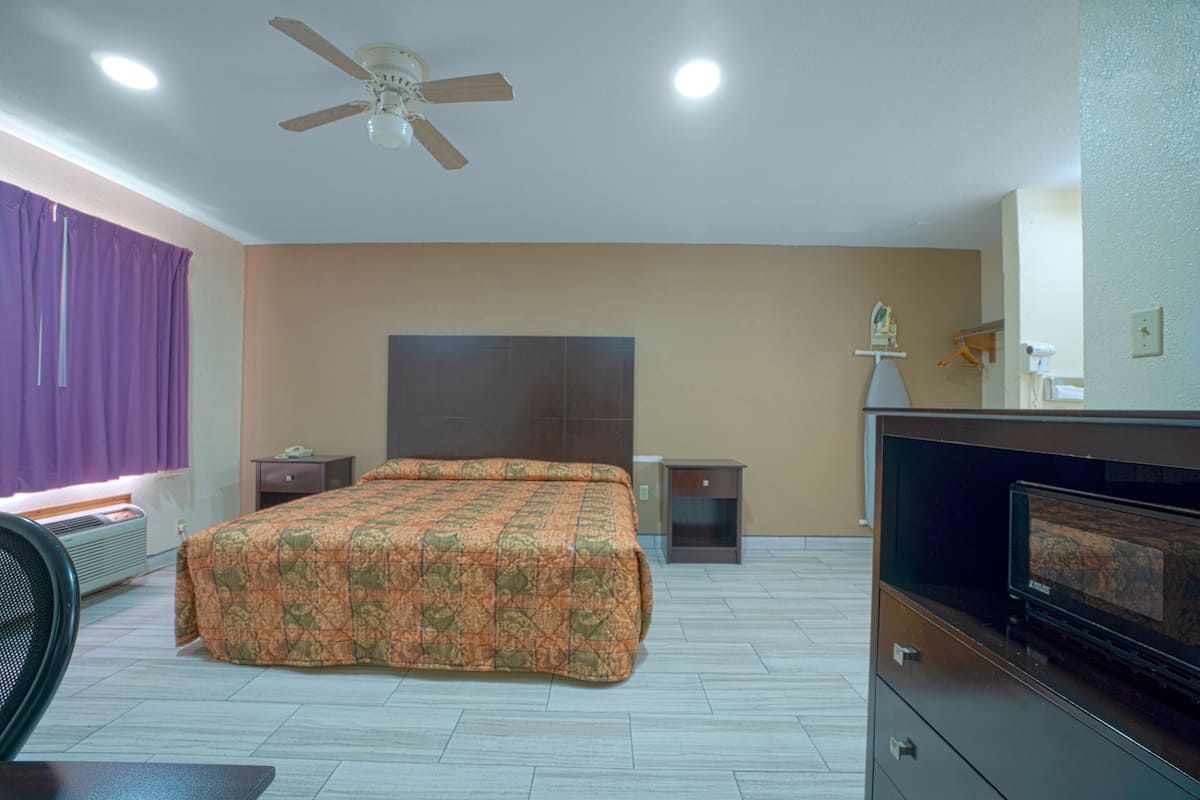 Ein Schlafzimmer mit Bett, Deckenventilator, Nachttisch, Kommode und Fernseher.