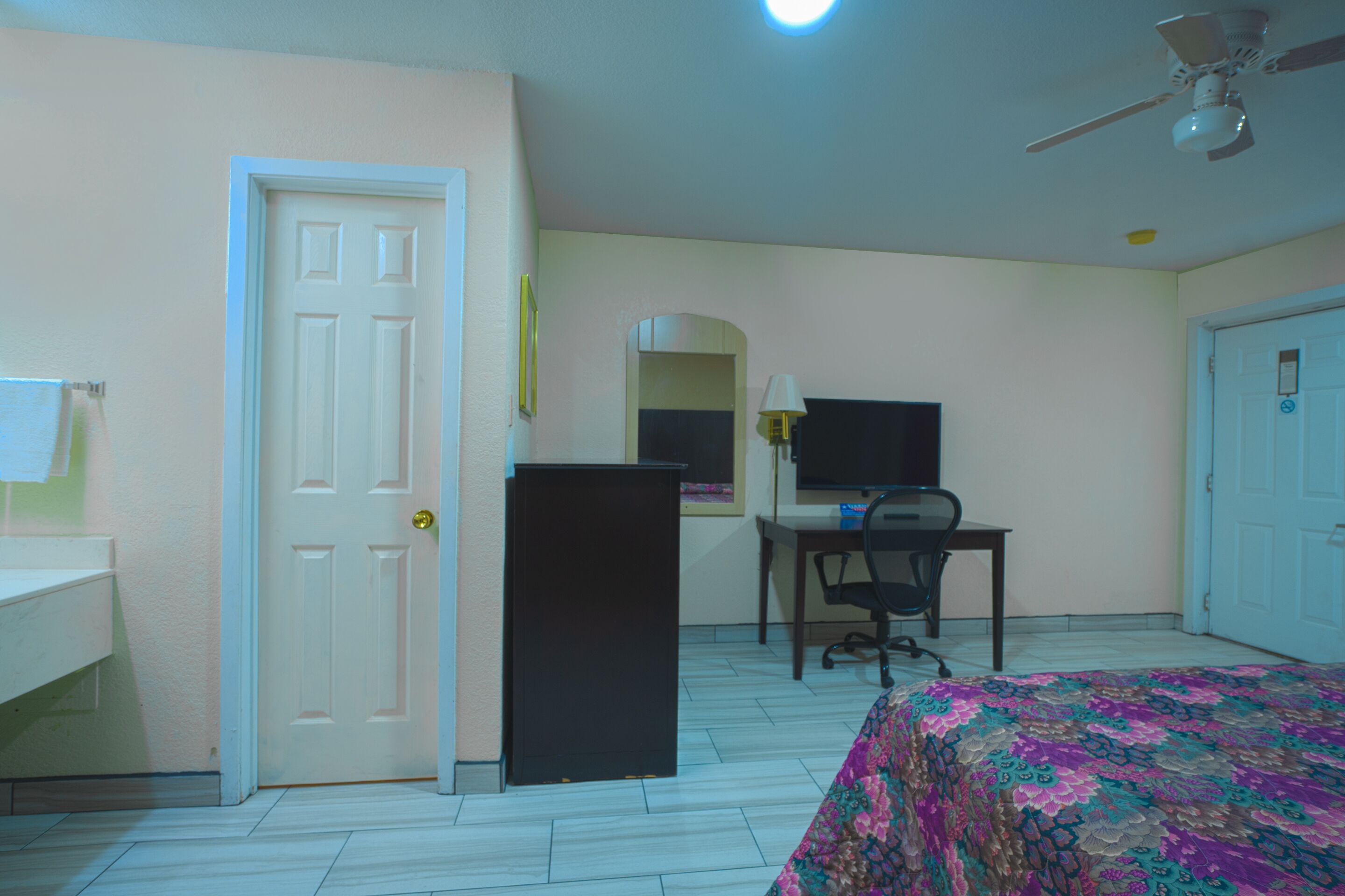 Un dormitorio con cama, escritorio, silla, televisor y una puerta.