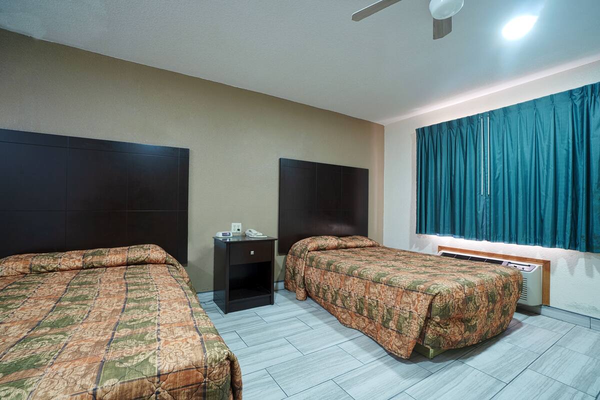 Ein Hotelzimmer mit zwei Betten, einem Nachttisch, einem Heizgerät und einem Fenster mit Vorhängen.