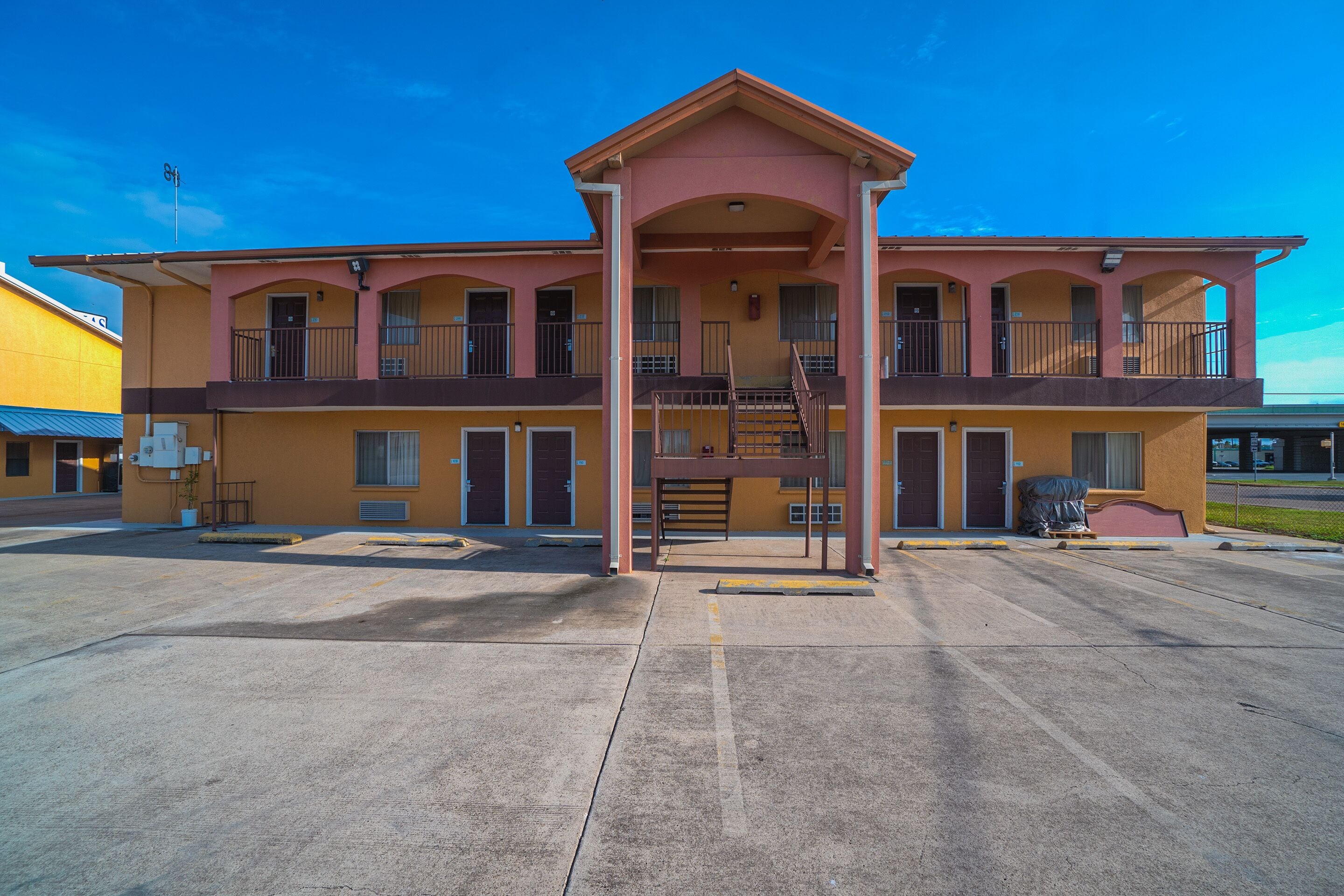 Un motel de dos pisos con un balcón central, varias habitaciones y un estacionamiento.