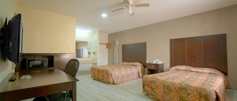 Una habitación de hotel con dos camas, un escritorio, una silla, un microondas, un ventilador de techo y una televisión.