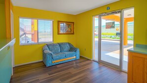 A room with yellow walls, a blue sofa, wooden flooring, and a sliding glass door leading outside. - Texas Inn San Benito near Harlingen (San Benito)