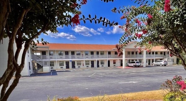 Un motel con estacionamiento central, una pasarela techada y un techo rojo.