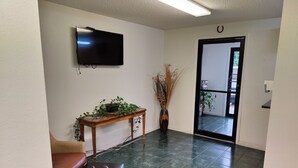 Una sala de estar con una televisión de pantalla plana, una mesa de centro de madera con plantas, un reposapiés de cuero marrón y una puerta que da a un balcón.