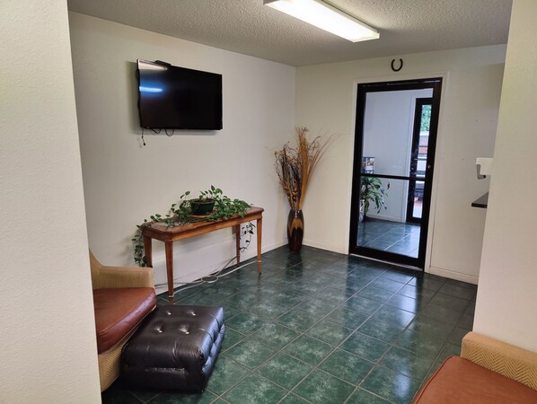 Una sala de estar con una televisión de pantalla plana, una mesa de centro de madera con plantas, un reposapiés de cuero marrón y una puerta que da a un balcón.