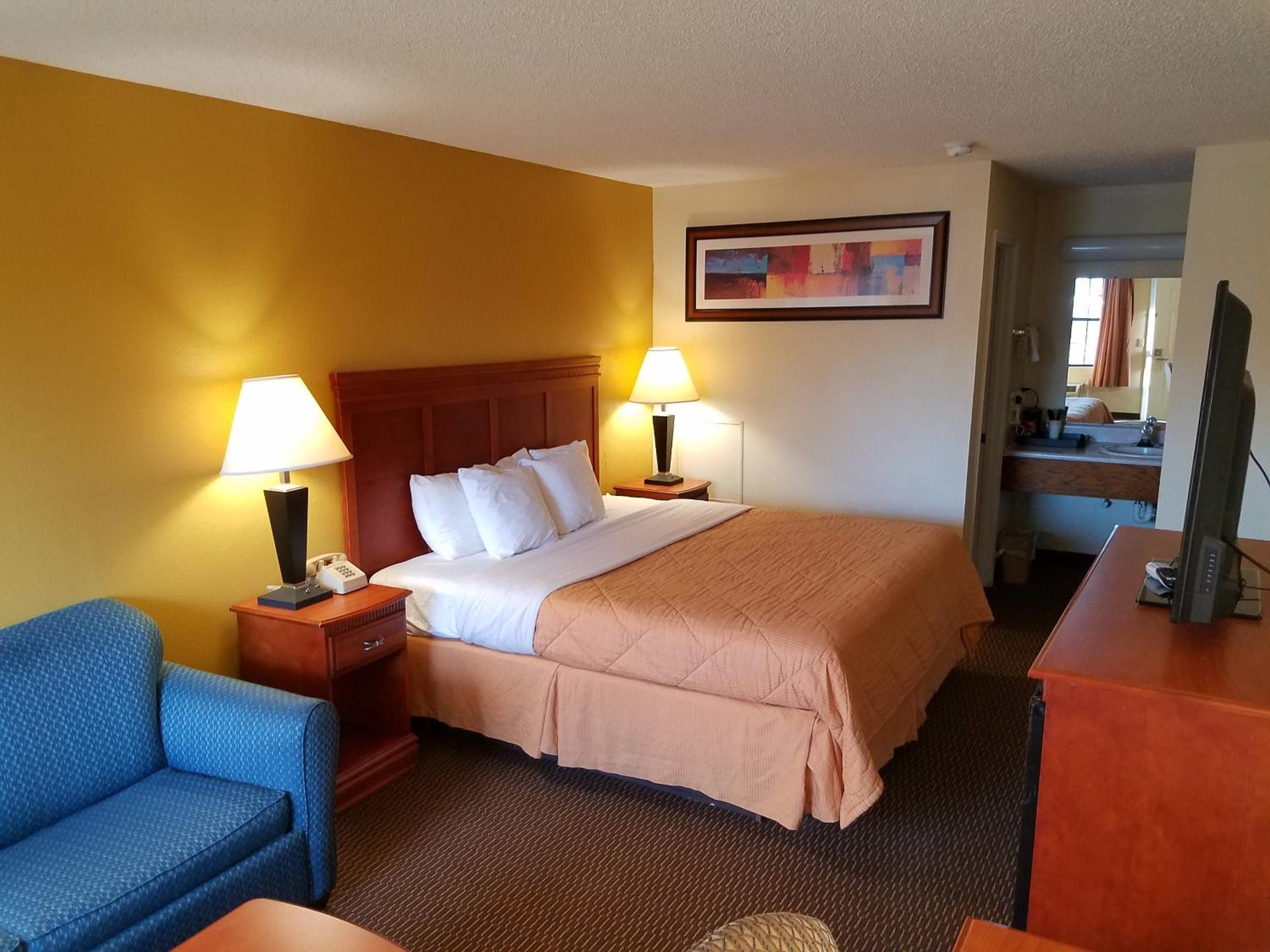 A hotel room with a bed, two bedside lamps, a chair, a desk, and a television.
