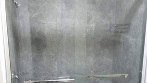 Cabina de ducha con paredes de vidrio, piso de baldosas y barandilla de metal.