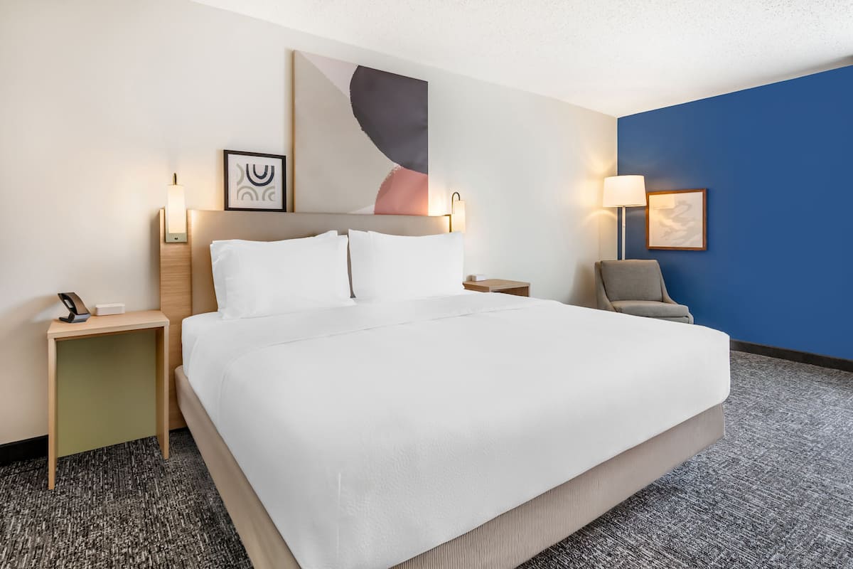 A hotel room with a large bed, two bedside tables, a chair, and artwork on the walls.