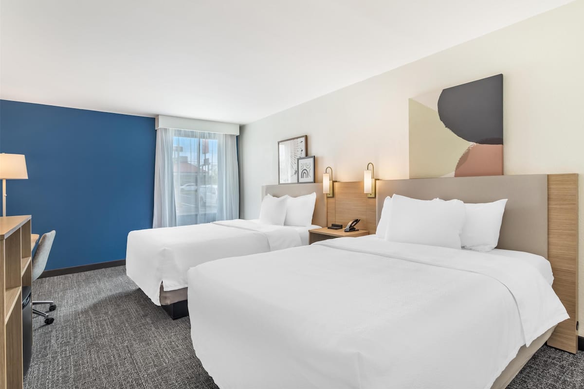 A hotel room with two beds, a desk, and a window with curtains.