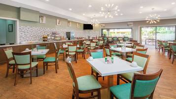 A spacious dining area with multiple tables and chairs, a buffet counter, and a television mounted on the wall.
