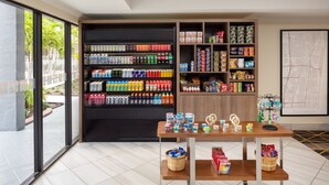 A modern retail space with shelves stocked with beverages and snacks, a wooden table with jars, and a large map on the wall. - Holiday Inn & Suites Boca Raton - North by IHG (Boca Raton)