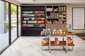Un espace de vente moderne, avec des étagères remplies de boissons et d’en-cas, une table en bois sur laquelle sont posés des bocaux, et une grande carte accrochée au mur.