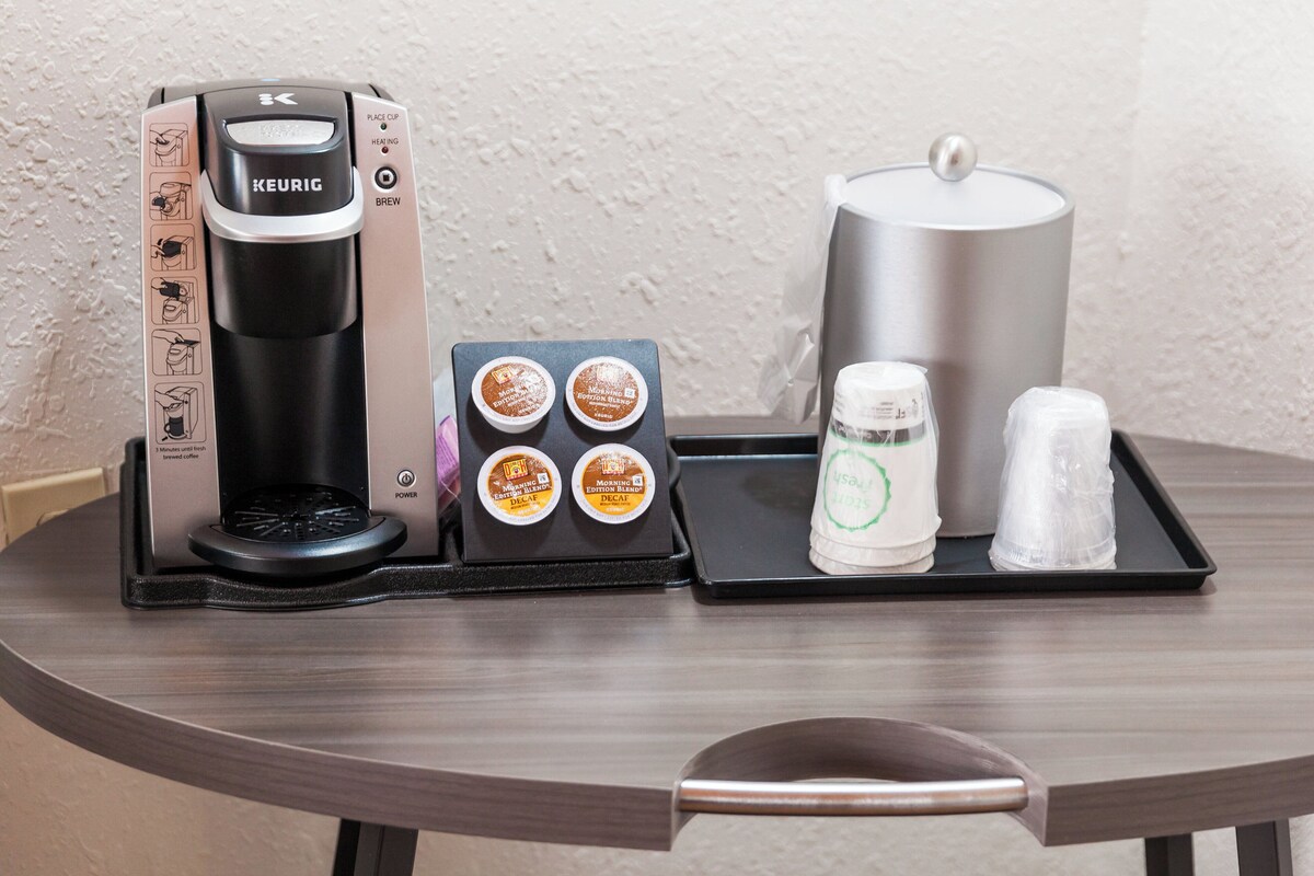Une machine à café Keurig, quatre dosettes de café, une bouteille d’eau et un thermos, le tout sur un plateau.