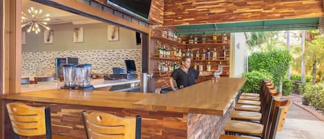 Zona de bar con mostrador de madera, taburetes y un camarero.