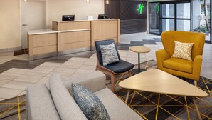 A modern hotel lobby with a reception desk, seating area, and large windows. - Holiday Inn & Suites Boca Raton - North by IHG (Boca Raton)