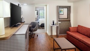 A hotel room with a flat-screen TV, a desk with a chair, a red sofa, and a small table with a coffee machine. - Holiday Inn & Suites Boca Raton - North by IHG (Boca Raton)