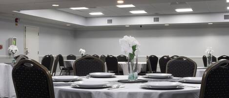 Un salón de conferencias con mesas redondas, sillas negras, manteles blancos y flores blancas en jarrones.