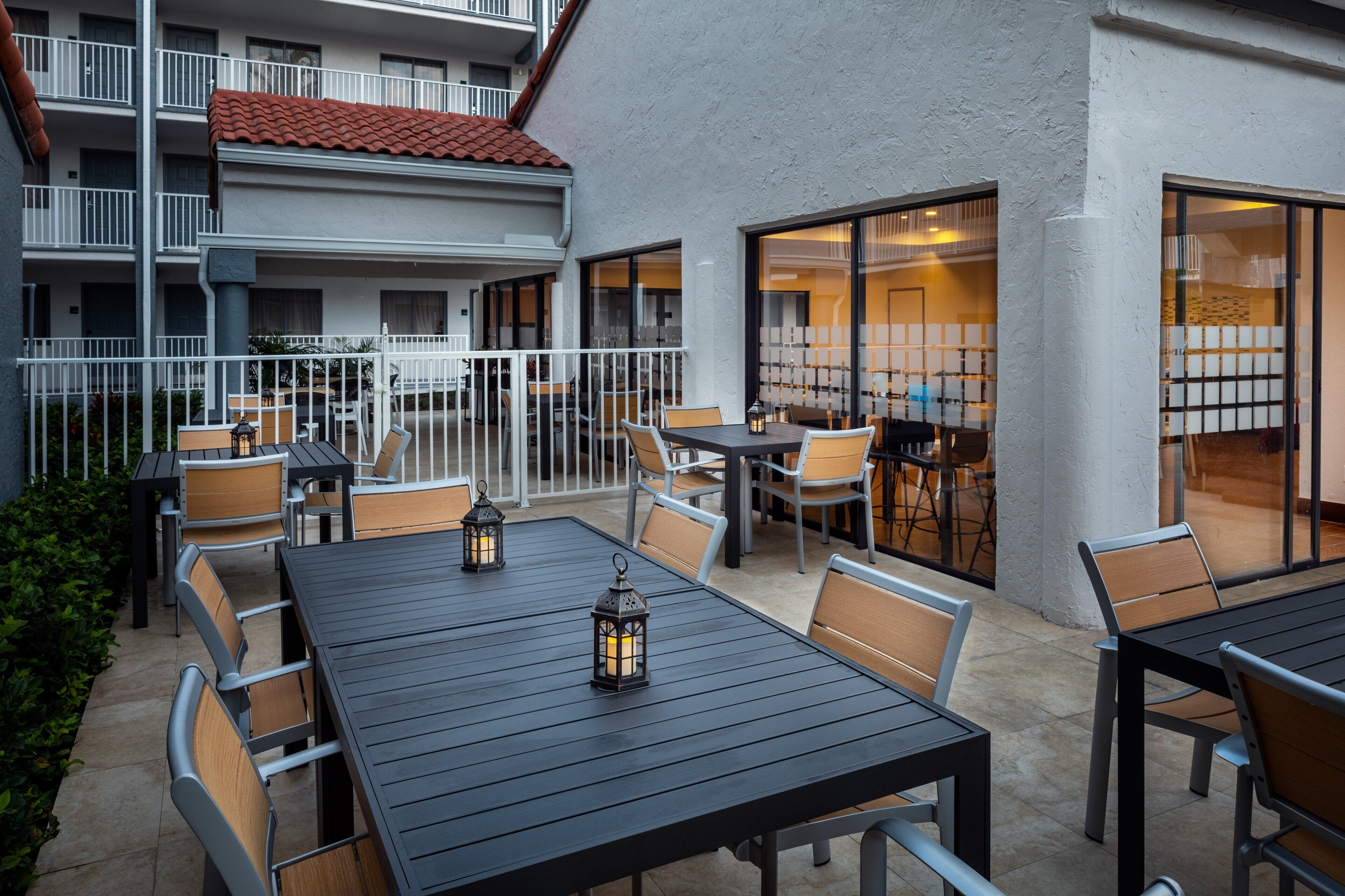 Ein Außenbereich mit Terrasse, Tischen, Stühlen, einem Geländer und einem Gebäude mit Ziegeldach und großen Fenstern.