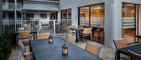Un espace extérieur aménagé en terrasse, avec des tables et des chaises, une rambarde et un bâtiment doté d’un toit en tuiles et de grandes fenêtres.