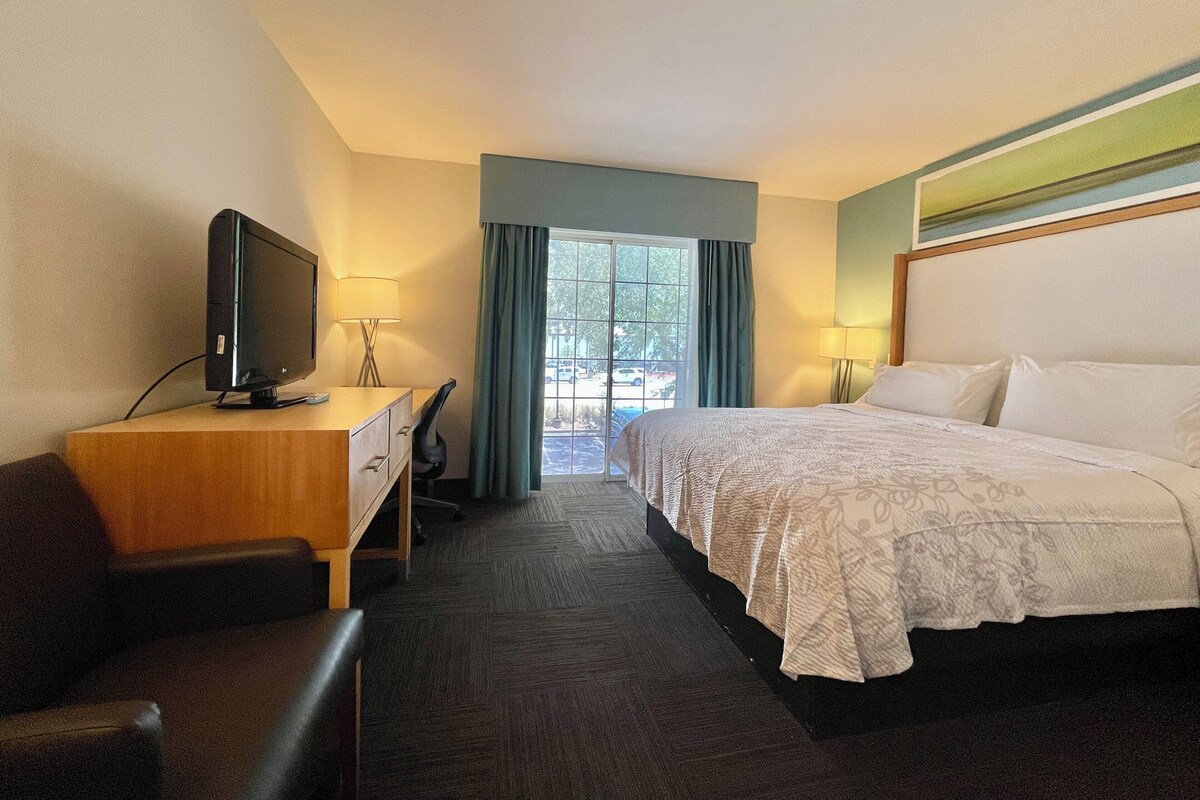 Una habitación de hotel con cama, escritorio con televisor, silla y ventana con cortinas.