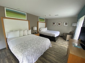 A hotel room with two beds, a television, a desk, and a window with a view.