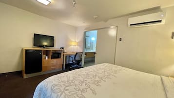 A hotel room with a bed, a desk with a television, a microwave, and a lamp.