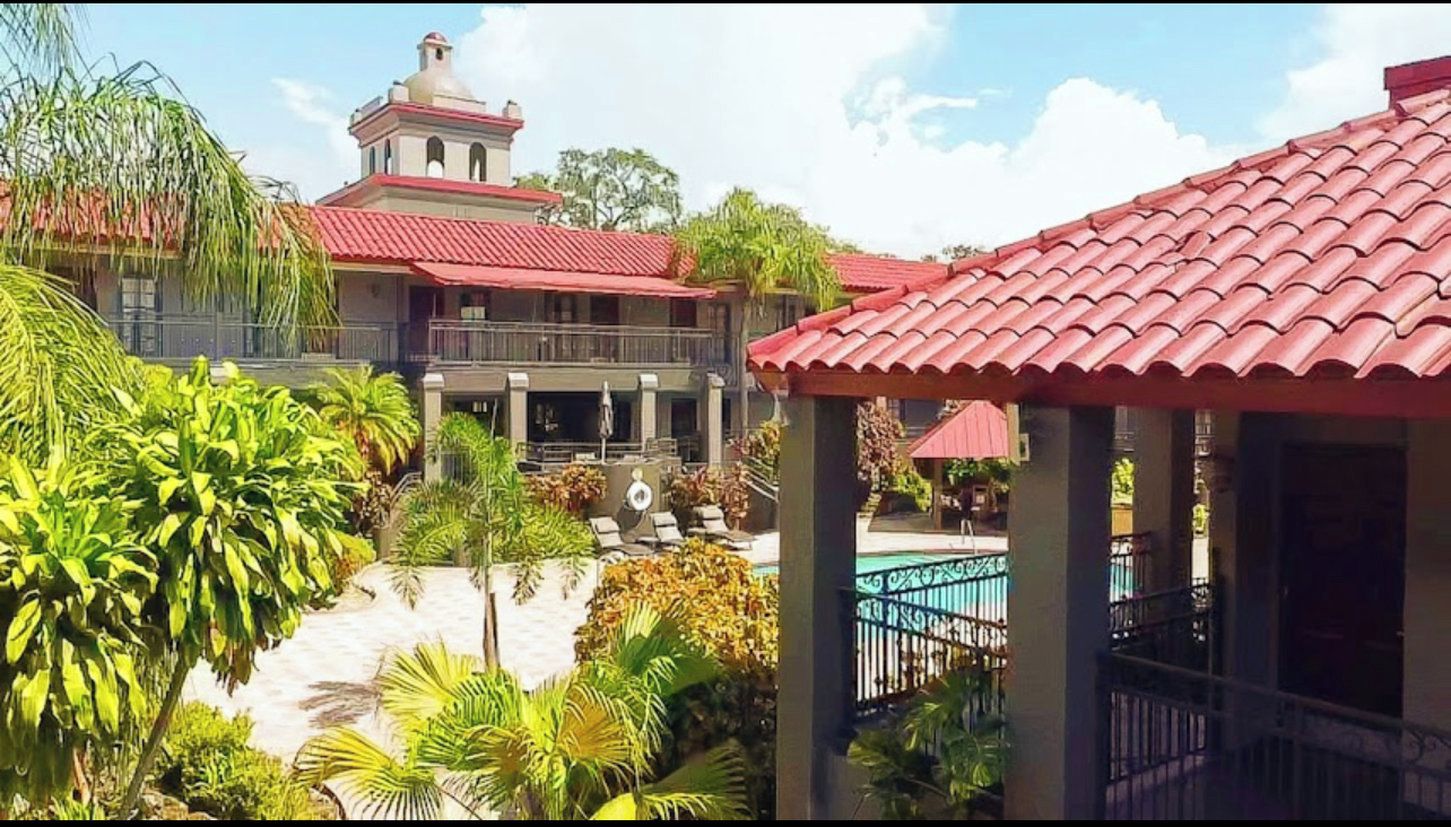 A hotel with a red-tiled roof, a pool area, and lush greenery.