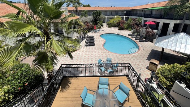 A pool area with lounge chairs and a table, surrounded by palm trees and a tiled deck.