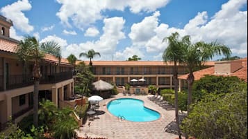 A pool area with a curved pool, lounge chairs, umbrellas, and palm trees.