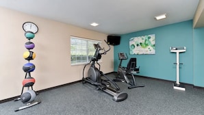 A gym with exercise equipment, a wall clock, and a window with blinds.