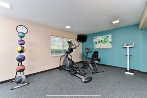 Een sportschool met trainingsapparatuur, een wandklok en een raam met jaloezieën.
