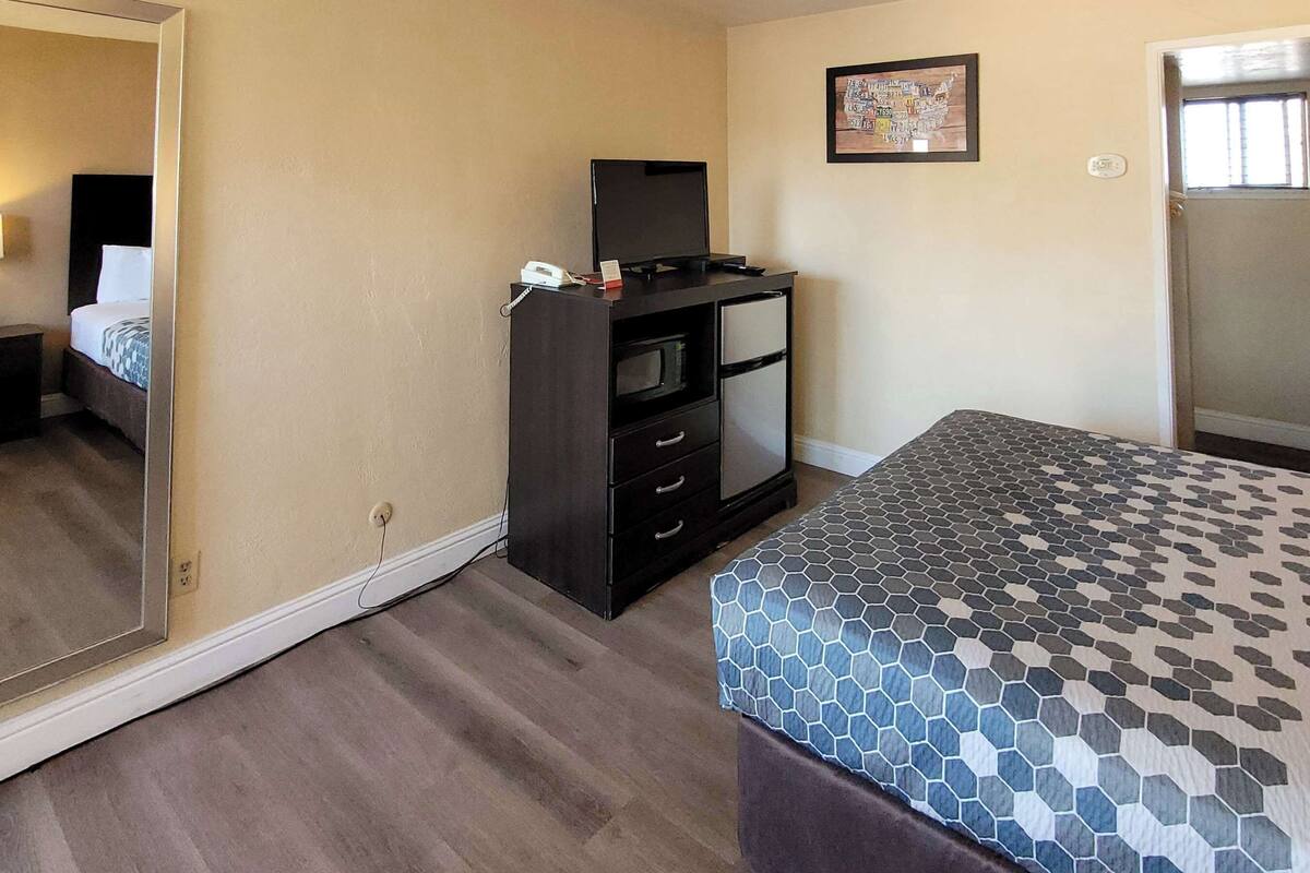 A hotel room with a bed, a TV on a cabinet, a mirror, and a map on the wall.