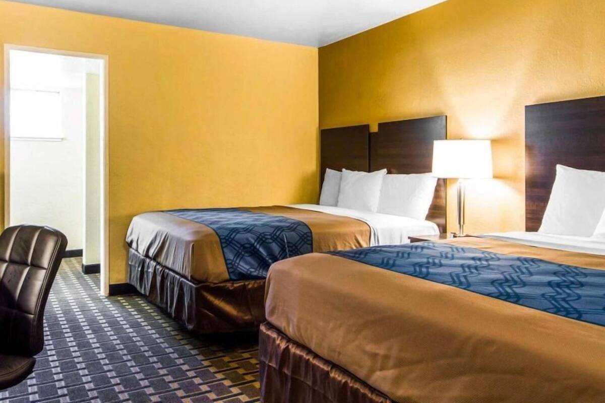 A hotel room with two beds, a chair, and a lamp.