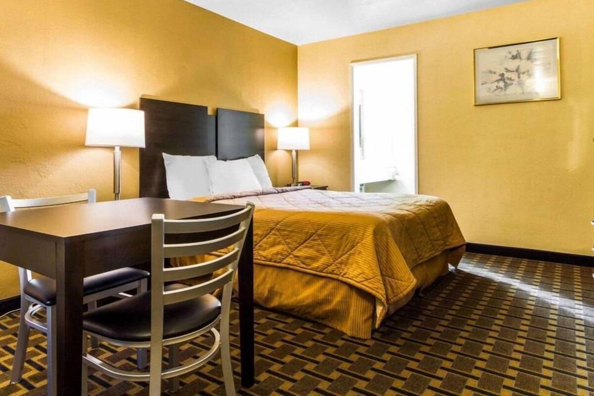 A hotel room with a bed, two bedside lamps, a desk with a chair, and a patterned floor.