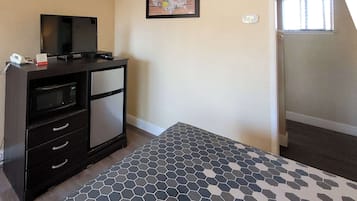 A hotel room with a dark wooden desk, a flat-screen TV, a microwave, and a hexagonal patterned rug.