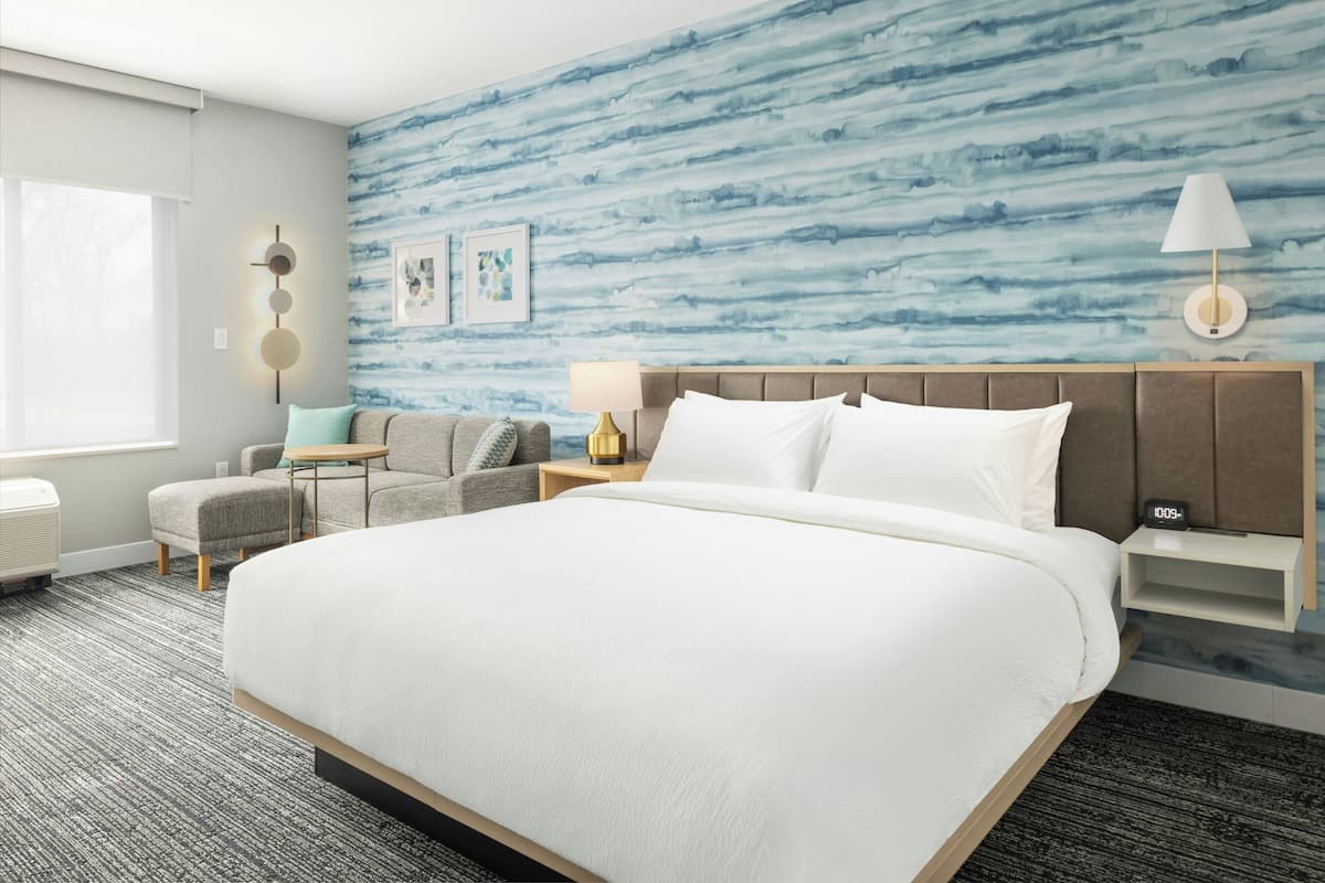 Una habitación de hotel con una cama grande, un sofá, una mesita y una mesita de noche con una lámpara.