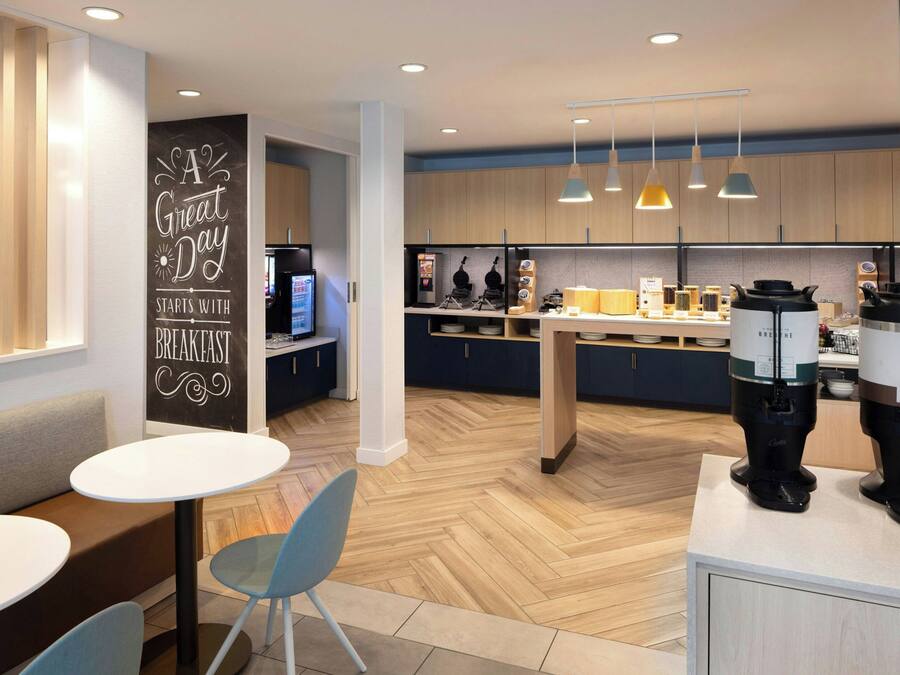 A modern kitchen with wooden cabinets, a herringbone floor, and a breakfast bar. There are two coffee makers on the counter.