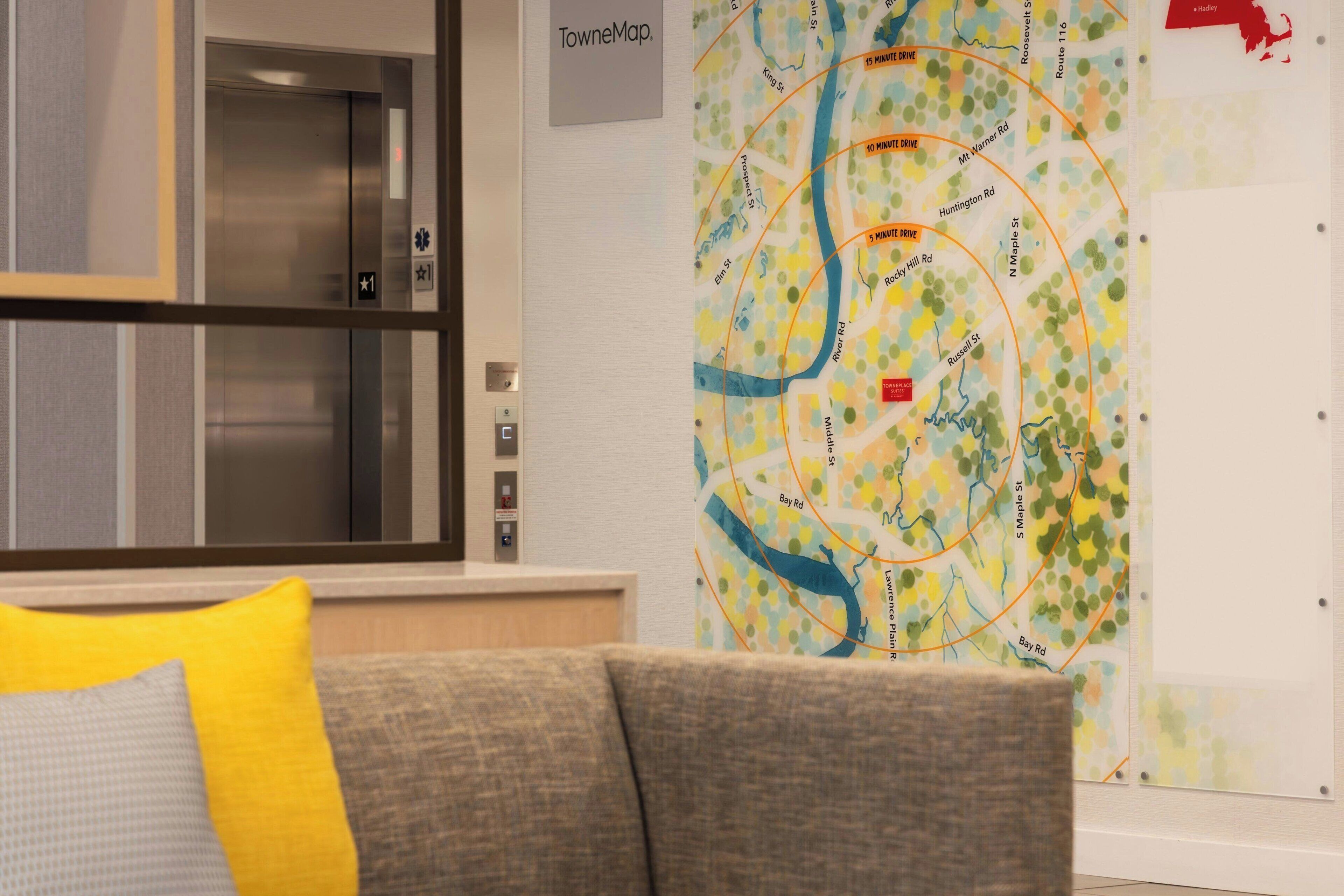 A hotel lobby with a map on the wall, an elevator, and a couch with a pillow.